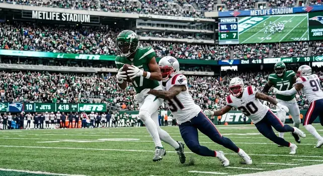 New York Jets wide receiver carrying the ball while being tackled by New England Patriots defenders during NFL regular season match at MetLife Stadium.